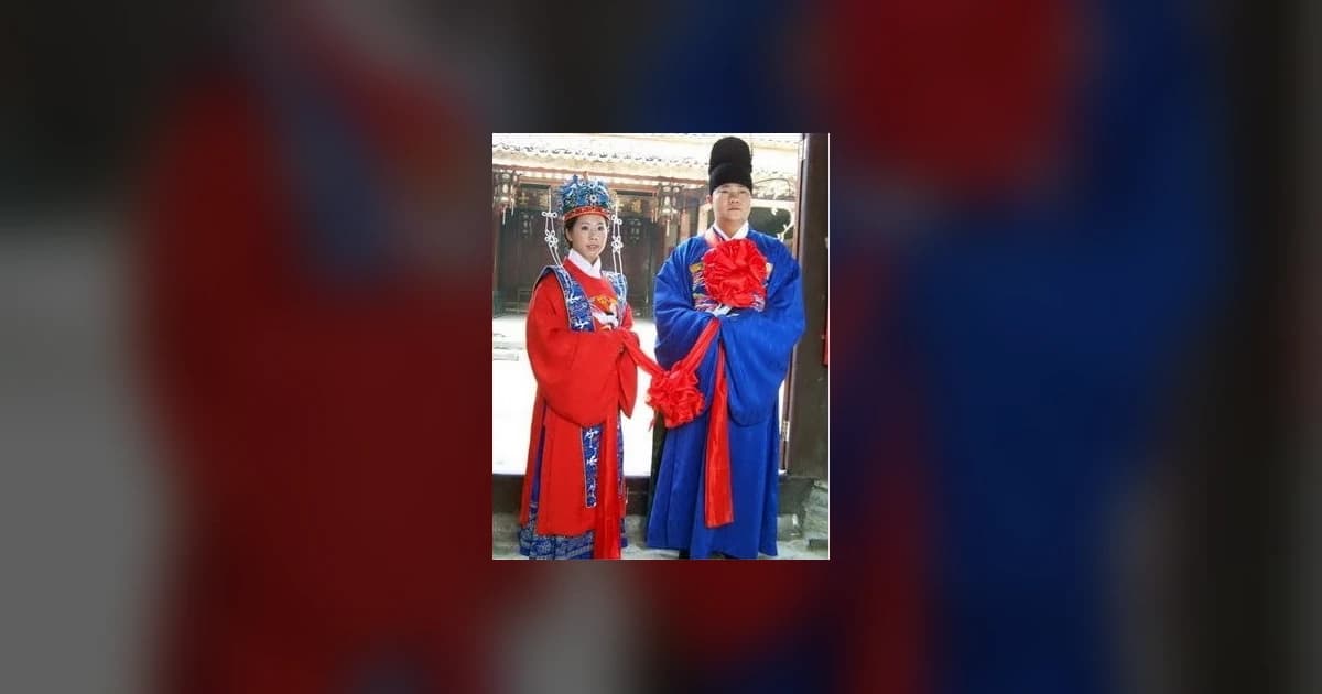 Traditional Chinese wedding couple in red and blue ceremonial clothing, centered over a dark blurred background